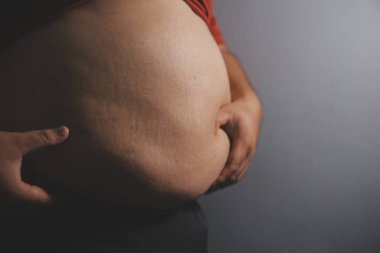 Asyalı şişman bir adam aynanın önünde vücuduna bakıyor. Aşırı göbek yağı, sağlıksız yaşam tarzı, diyet konsepti.