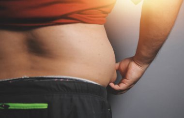 Asyalı şişman bir adam aynanın önünde vücuduna bakıyor. Aşırı göbek yağı, sağlıksız yaşam tarzı, diyet konsepti.