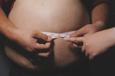 Asyalı şişman bir adam aynanın önünde vücuduna bakıyor. Aşırı göbek yağı, sağlıksız yaşam tarzı, diyet konsepti.