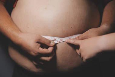 Asyalı şişman bir adam aynanın önünde vücuduna bakıyor. Aşırı göbek yağı, sağlıksız yaşam tarzı, diyet konsepti.