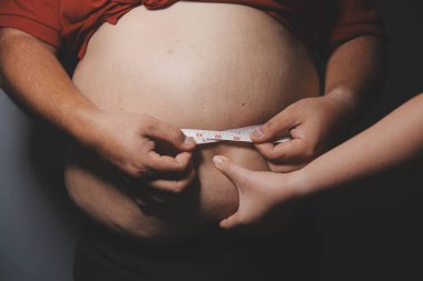 Asyalı şişman bir adam aynanın önünde vücuduna bakıyor. Aşırı göbek yağı, sağlıksız yaşam tarzı, diyet konsepti.