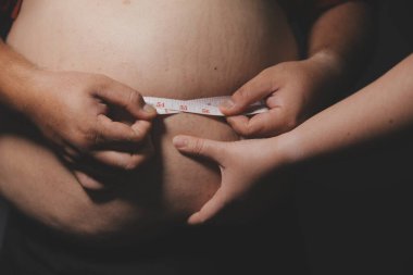 Asyalı şişman bir adam aynanın önünde vücuduna bakıyor. Aşırı göbek yağı, sağlıksız yaşam tarzı, diyet konsepti.