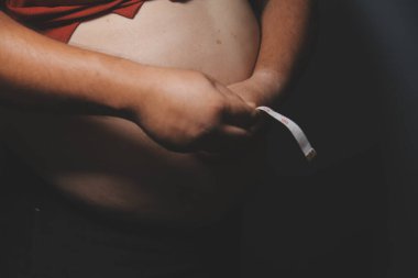 Asyalı şişman bir adam aynanın önünde vücuduna bakıyor. Aşırı göbek yağı, sağlıksız yaşam tarzı, diyet konsepti.