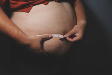 Asyalı şişman bir adam aynanın önünde vücuduna bakıyor. Aşırı göbek yağı, sağlıksız yaşam tarzı, diyet konsepti.