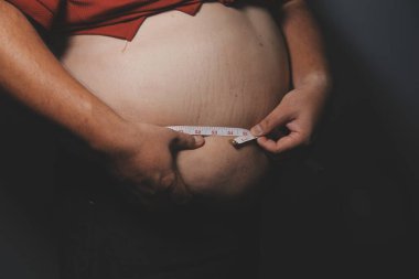 Asyalı şişman bir adam aynanın önünde vücuduna bakıyor. Aşırı göbek yağı, sağlıksız yaşam tarzı, diyet konsepti.