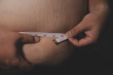 Asyalı şişman bir adam aynanın önünde vücuduna bakıyor. Aşırı göbek yağı, sağlıksız yaşam tarzı, diyet konsepti.