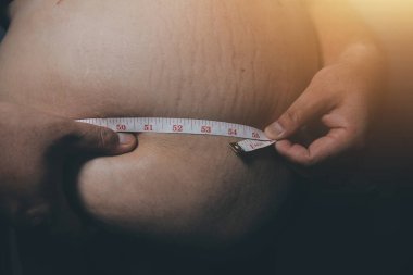 Asyalı şişman bir adam aynanın önünde vücuduna bakıyor. Aşırı göbek yağı, sağlıksız yaşam tarzı, diyet konsepti.