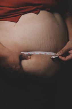 Asyalı şişman bir adam aynanın önünde vücuduna bakıyor. Aşırı göbek yağı, sağlıksız yaşam tarzı, diyet konsepti.