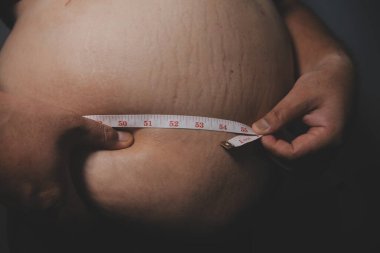 Asyalı şişman bir adam aynanın önünde vücuduna bakıyor. Aşırı göbek yağı, sağlıksız yaşam tarzı, diyet konsepti.