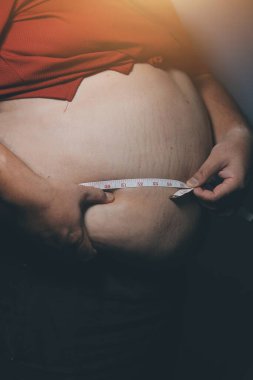 Asyalı şişman bir adam aynanın önünde vücuduna bakıyor. Aşırı göbek yağı, sağlıksız yaşam tarzı, diyet konsepti.