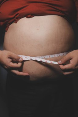 Asyalı şişman bir adam aynanın önünde vücuduna bakıyor. Aşırı göbek yağı, sağlıksız yaşam tarzı, diyet konsepti.