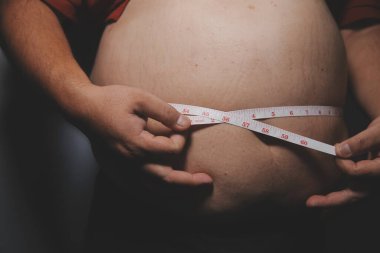 Asyalı şişman bir adam aynanın önünde vücuduna bakıyor. Aşırı göbek yağı, sağlıksız yaşam tarzı, diyet konsepti.