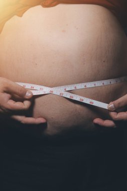 Asyalı şişman bir adam aynanın önünde vücuduna bakıyor. Aşırı göbek yağı, sağlıksız yaşam tarzı, diyet konsepti.