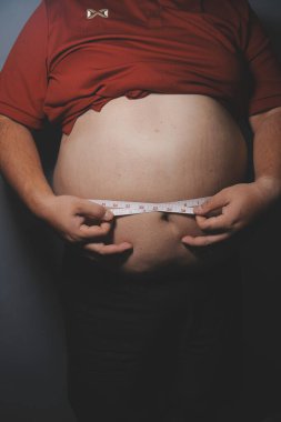 Asyalı şişman bir adam aynanın önünde vücuduna bakıyor. Aşırı göbek yağı, sağlıksız yaşam tarzı, diyet konsepti.