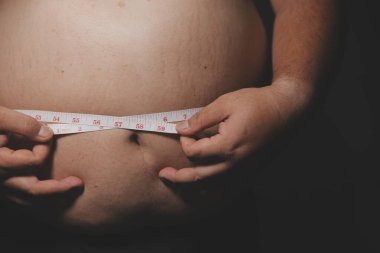 Asyalı şişman bir adam aynanın önünde vücuduna bakıyor. Aşırı göbek yağı, sağlıksız yaşam tarzı, diyet konsepti.