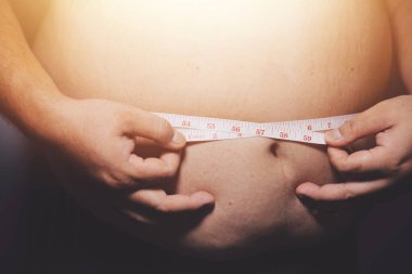 Asyalı şişman bir adam aynanın önünde vücuduna bakıyor. Aşırı göbek yağı, sağlıksız yaşam tarzı, diyet konsepti.