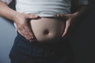 Asyalı şişman bir adam aynanın önünde vücuduna bakıyor. Aşırı göbek yağı, sağlıksız yaşam tarzı, diyet konsepti.