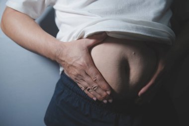 Asyalı şişman bir adam aynanın önünde vücuduna bakıyor. Aşırı göbek yağı, sağlıksız yaşam tarzı, diyet konsepti.