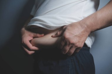 Asyalı şişman bir adam aynanın önünde vücuduna bakıyor. Aşırı göbek yağı, sağlıksız yaşam tarzı, diyet konsepti.