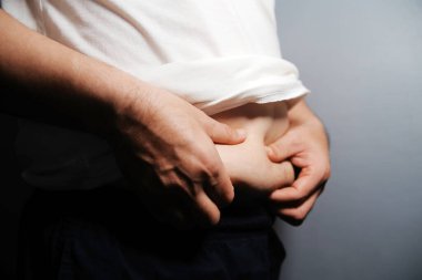 Asyalı şişman bir adam aynanın önünde vücuduna bakıyor. Aşırı göbek yağı, sağlıksız yaşam tarzı, diyet konsepti.