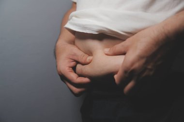 Asyalı şişman bir adam aynanın önünde vücuduna bakıyor. Aşırı göbek yağı, sağlıksız yaşam tarzı, diyet konsepti.