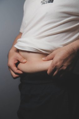 Asyalı şişman bir adam aynanın önünde vücuduna bakıyor. Aşırı göbek yağı, sağlıksız yaşam tarzı, diyet konsepti.