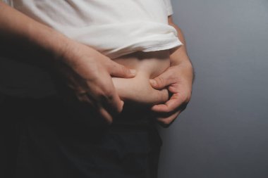 Asyalı şişman bir adam aynanın önünde vücuduna bakıyor. Aşırı göbek yağı, sağlıksız yaşam tarzı, diyet konsepti.