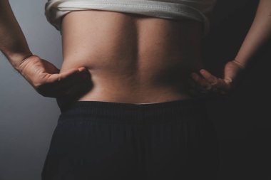 Asyalı şişman bir adam aynanın önünde vücuduna bakıyor. Aşırı göbek yağı, sağlıksız yaşam tarzı, diyet konsepti.