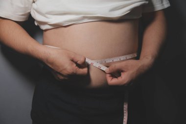 Asyalı şişman bir adam aynanın önünde vücuduna bakıyor. Aşırı göbek yağı, sağlıksız yaşam tarzı, diyet konsepti.