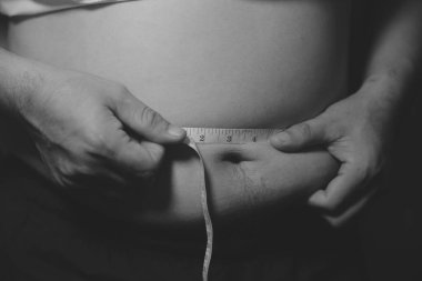 Asyalı şişman bir adam aynanın önünde vücuduna bakıyor. Aşırı göbek yağı, sağlıksız yaşam tarzı, diyet konsepti.