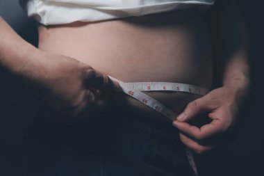 Asyalı şişman bir adam aynanın önünde vücuduna bakıyor. Aşırı göbek yağı, sağlıksız yaşam tarzı, diyet konsepti.