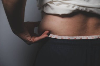 Asyalı şişman bir adam aynanın önünde vücuduna bakıyor. Aşırı göbek yağı, sağlıksız yaşam tarzı, diyet konsepti.