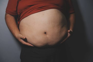 Asyalı şişman bir adam aynanın önünde vücuduna bakıyor. Aşırı göbek yağı, sağlıksız yaşam tarzı, diyet konsepti.