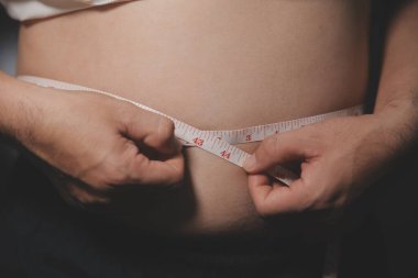 Asyalı şişman bir adam aynanın önünde vücuduna bakıyor. Aşırı göbek yağı, sağlıksız yaşam tarzı, diyet konsepti.