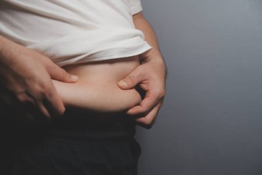 Asyalı şişman bir adam aynanın önünde vücuduna bakıyor. Aşırı göbek yağı, sağlıksız yaşam tarzı, diyet konsepti.