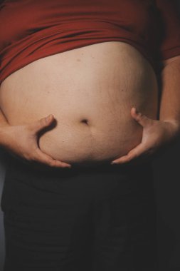 Asyalı şişman bir adam aynanın önünde vücuduna bakıyor. Aşırı göbek yağı, sağlıksız yaşam tarzı, diyet konsepti.