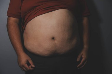 Asyalı şişman bir adam aynanın önünde vücuduna bakıyor. Aşırı göbek yağı, sağlıksız yaşam tarzı, diyet konsepti.