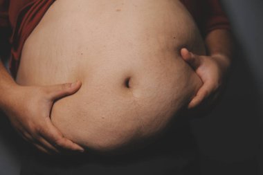 Asyalı şişman bir adam aynanın önünde vücuduna bakıyor. Aşırı göbek yağı, sağlıksız yaşam tarzı, diyet konsepti.