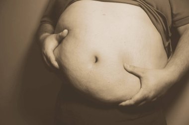 Asyalı şişman bir adam aynanın önünde vücuduna bakıyor. Aşırı göbek yağı, sağlıksız yaşam tarzı, diyet konsepti.