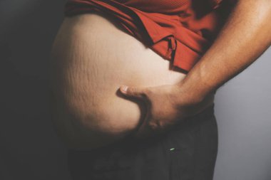 Asyalı şişman bir adam aynanın önünde vücuduna bakıyor. Aşırı göbek yağı, sağlıksız yaşam tarzı, diyet konsepti.