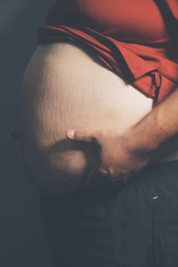 Asyalı şişman bir adam aynanın önünde vücuduna bakıyor. Aşırı göbek yağı, sağlıksız yaşam tarzı, diyet konsepti.