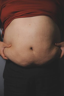 Asyalı şişman bir adam aynanın önünde vücuduna bakıyor. Aşırı göbek yağı, sağlıksız yaşam tarzı, diyet konsepti.