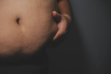 Asyalı şişman bir adam aynanın önünde vücuduna bakıyor. Aşırı göbek yağı, sağlıksız yaşam tarzı, diyet konsepti.