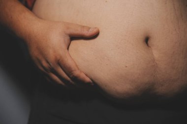 Asyalı şişman bir adam aynanın önünde vücuduna bakıyor. Aşırı göbek yağı, sağlıksız yaşam tarzı, diyet konsepti.