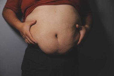 Asyalı şişman bir adam aynanın önünde vücuduna bakıyor. Aşırı göbek yağı, sağlıksız yaşam tarzı, diyet konsepti.