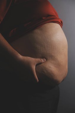 Asyalı şişman bir adam aynanın önünde vücuduna bakıyor. Aşırı göbek yağı, sağlıksız yaşam tarzı, diyet konsepti.