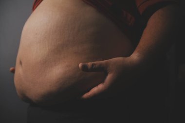 Asyalı şişman bir adam aynanın önünde vücuduna bakıyor. Aşırı göbek yağı, sağlıksız yaşam tarzı, diyet konsepti.