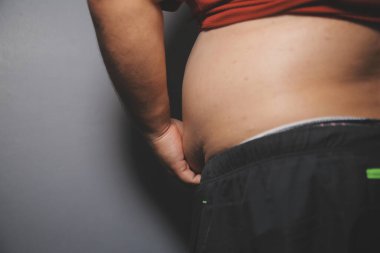 Asyalı şişman bir adam aynanın önünde vücuduna bakıyor. Aşırı göbek yağı, sağlıksız yaşam tarzı, diyet konsepti.