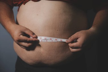 Asyalı şişman bir adam aynanın önünde vücuduna bakıyor. Aşırı göbek yağı, sağlıksız yaşam tarzı, diyet konsepti.