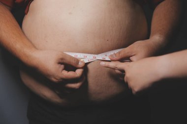 Asyalı şişman bir adam aynanın önünde vücuduna bakıyor. Aşırı göbek yağı, sağlıksız yaşam tarzı, diyet konsepti.